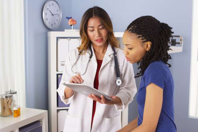 Asian Female Doctor speaking With Female African American Patient