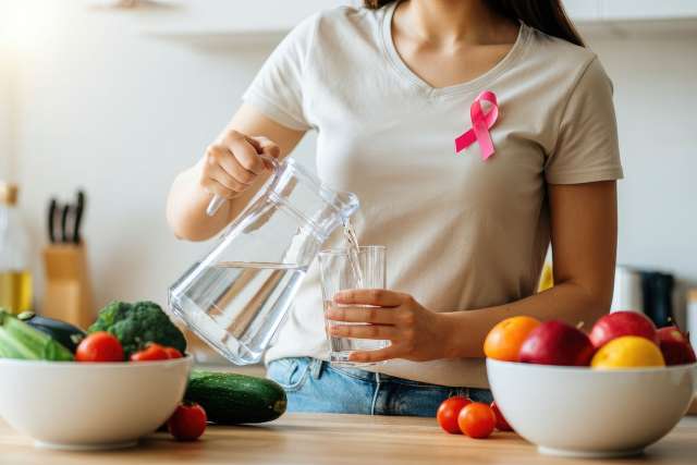 Woman with cancer awareness ribbon pouring water into glass