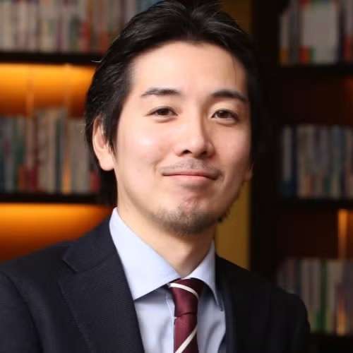 headshot of Dr. Yusuke Tsugawa wearing black suite with bookshelves in the background