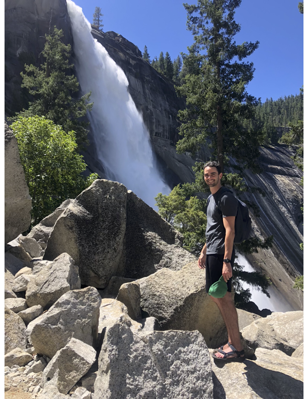 Man standing on rocks at a waterfall surrounded by trees.