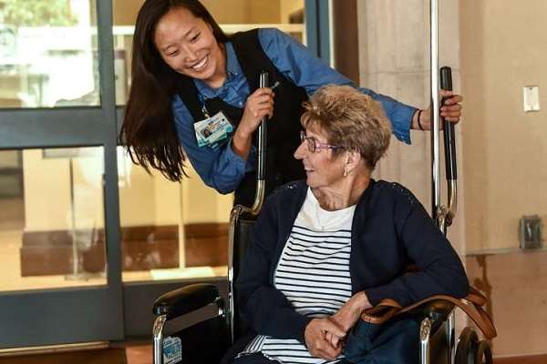 A nurse stands behind a patient in a wheelchair.
