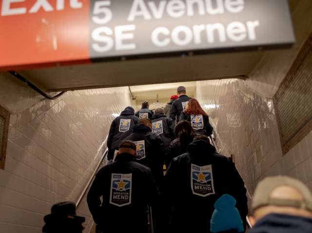 A group walking up subway steps while wearing Operation Mend jackets