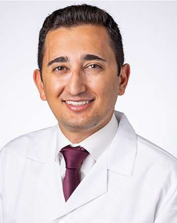 A man wearing a white lab coat and a burgundy tie against a white background.