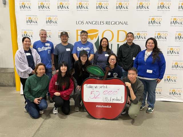 Group of people posing before Los Angeles Regional Food Bank backdrop holding large red apple sign