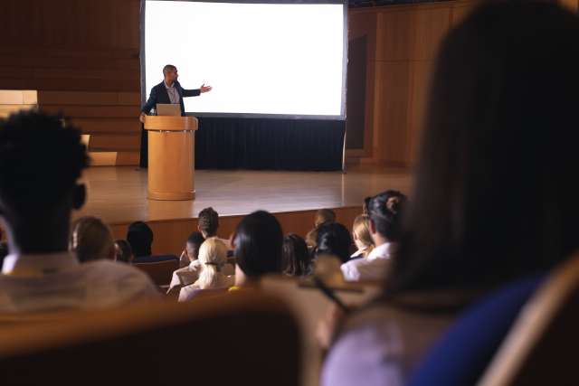 A man standing on a stage, giving a presentation to an auditorium.
