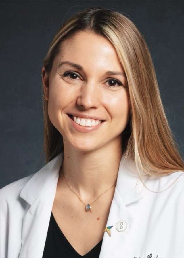 Smiling woman wearing a white coat against dark background.