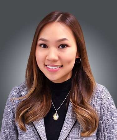  A headshot of Nancy Tran, a smiling woman with long brown hair, wearing a black turtleneck, a patterned blazer, and a pendant necklace.