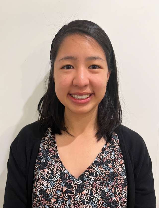 Tammy Le stands in front of a plain background, wearing a floral blouse and cardigan.