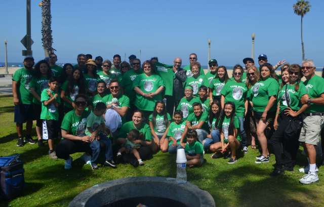 A large group of people wearing green shirts gather outdoors near the beach.