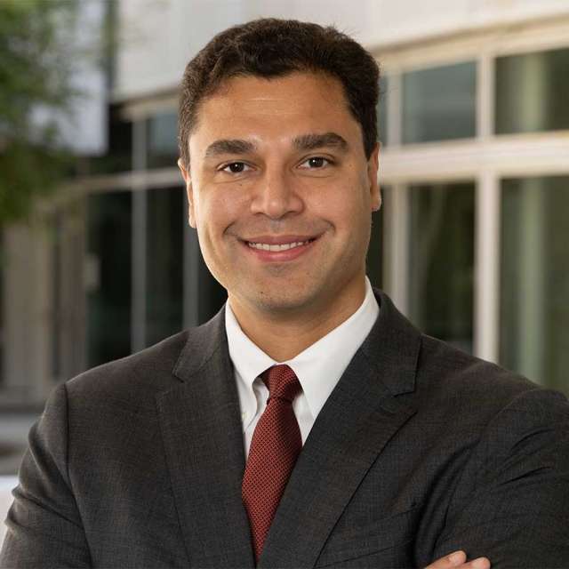 Dr. John V. Hegde posing outside, wearing a dark coat and smiling.