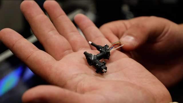 Two hands holding small black electronic components with thin wires