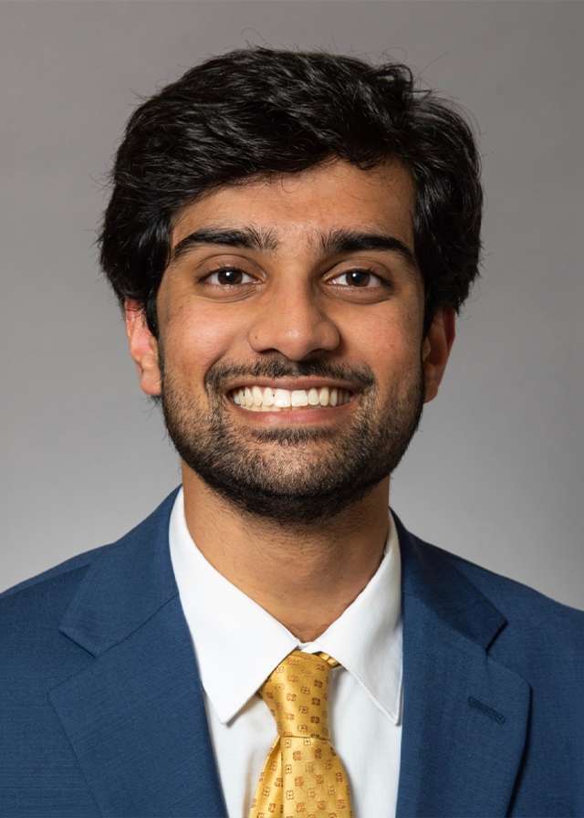 Smiling man in blue suit and gold tie against a gray background