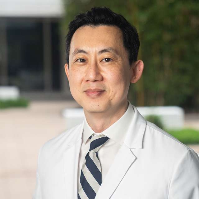 Dr. Robert K. Chin posing outside, wearing a white coat and smiling.