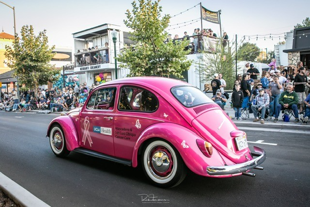 Pink vintage Volkswagen Beetle driving past spectators during a street parade.
