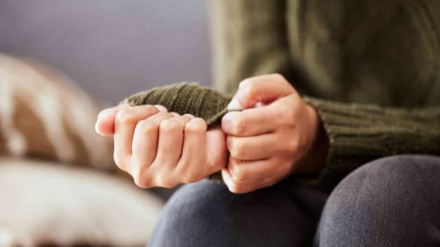 A person in a green sweater anxiously clasping their hands together.