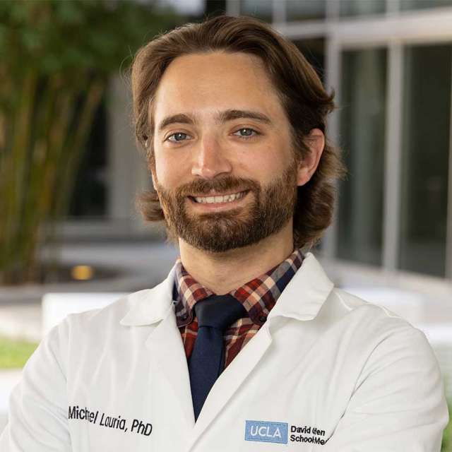 Dr. Michael Lauria posing outside, wearing a white coat and smiling.