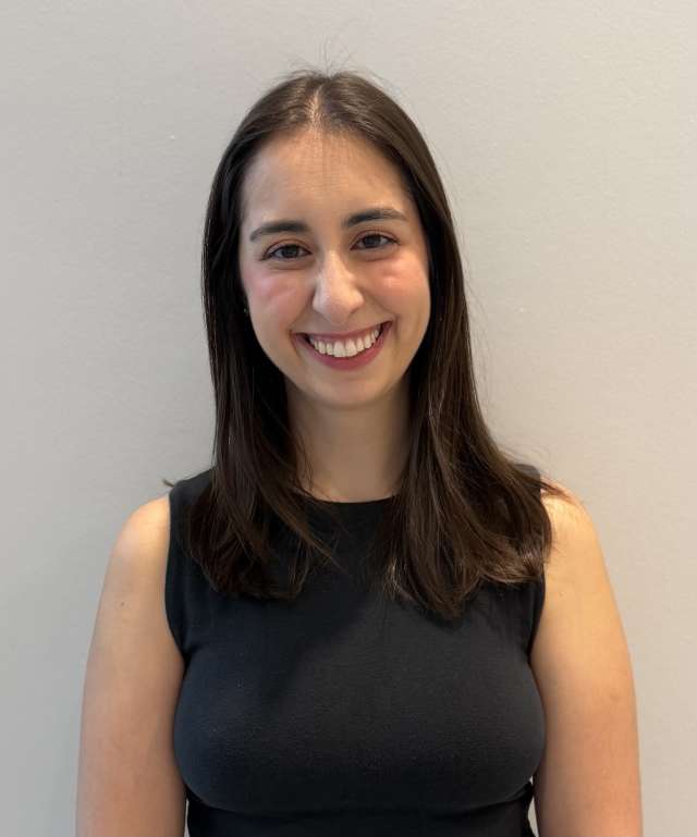 Smiling woman in black sleeveless top against plain light wall.