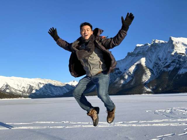 Harrison jumps joyfully on a snowy landscape with mountains in the background.