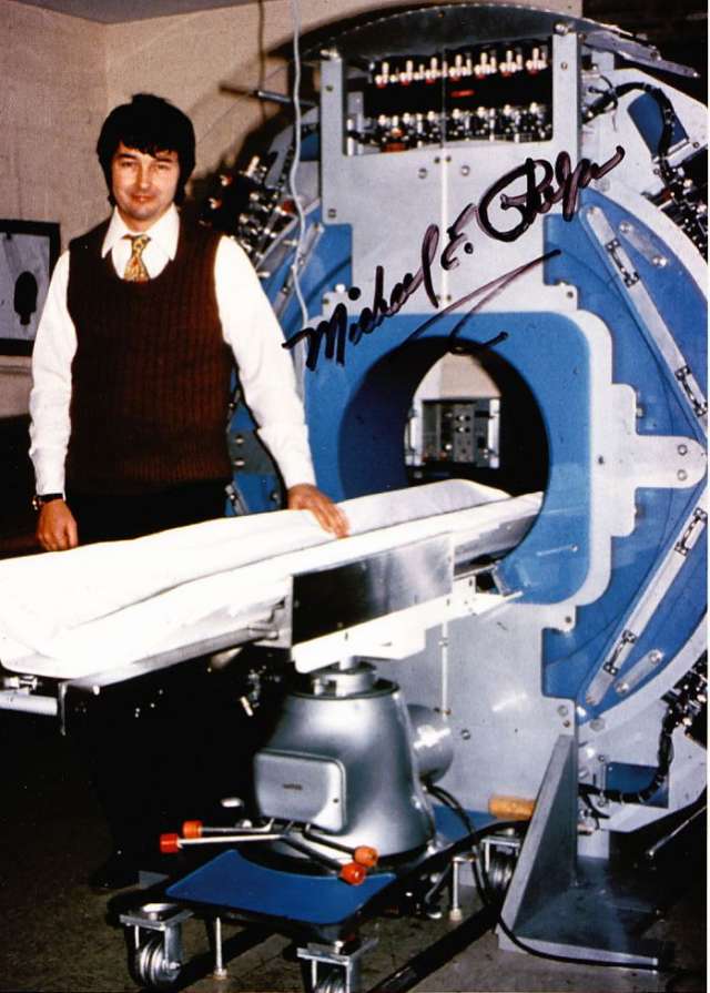 Michael Phelps in a brown vest standing beside the first PET scanner.