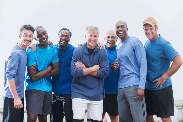 Diverse group of men wearing casual blue shirts, standing together outdoors.