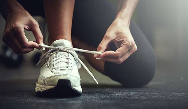 A close-up of a person tying the white laces of a white running shoe while wearing black athletic pants.