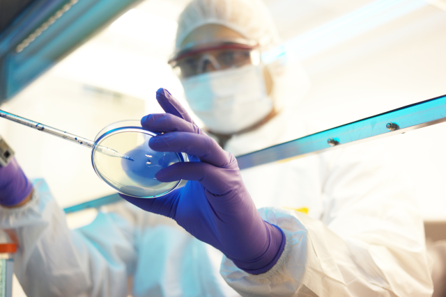 Scientist in PPE handling a petri dish in a lab setting.