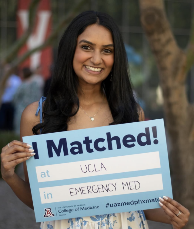 A person holds a sign that reads "I Matched! at UCLA in EMERGENCY MED."