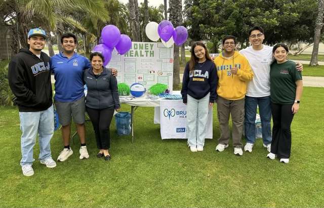 A group of seven people posing outdoors by a health information booth with balloons.