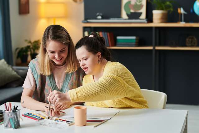 Girl with Down Syndrome coloring with her teacher