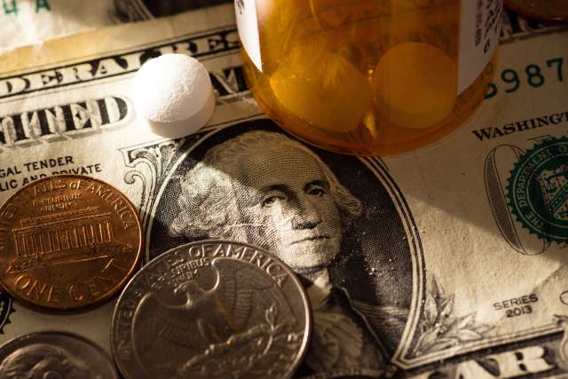 Pills beside cash, including coins and a one-dollar bill, on a flat surface.