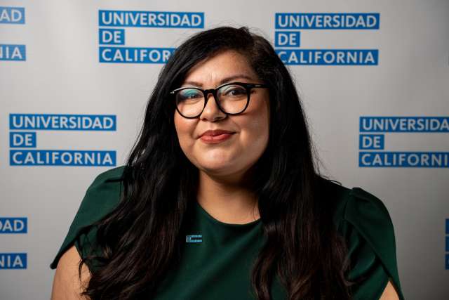 Olivia Diaz, DAPM Team Member, poses in front of Universidad de California step and repeat