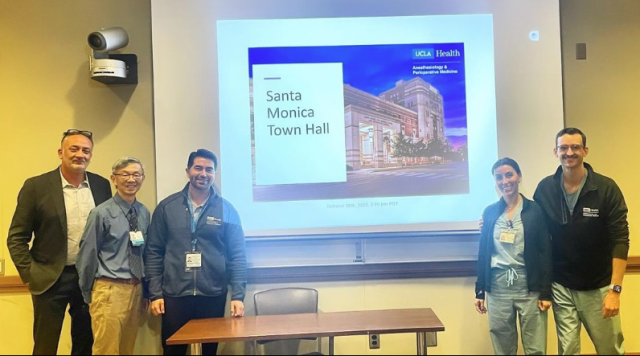 Five members of the DAPM Team posing in front of a projector at SM Town Hall in December 2023.