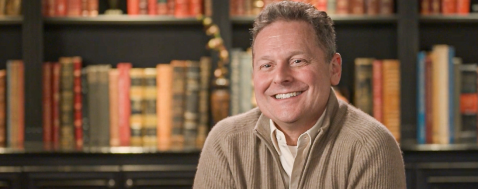 Dr. Brandon Koretz sitting in front of a full bookshelf, smiling