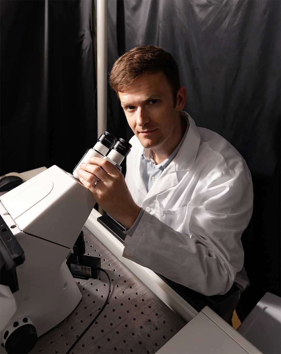 Aaron Meyer, associate professor sitting at a microscope.