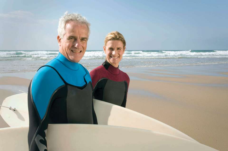 Man and woman in wetsuits on the beach carrying surfboards