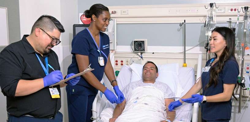 Nurses assist a patient lying in a hospital bed in a medical setting.