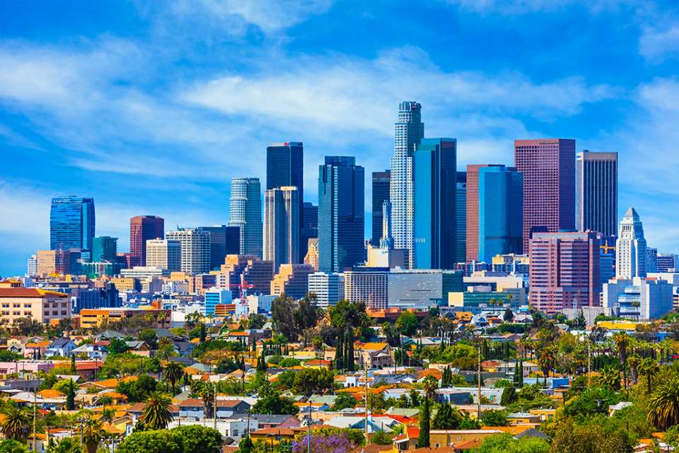 the Downtown Los Angeles skyline with several sky scapers and smaller buildings with green foliage