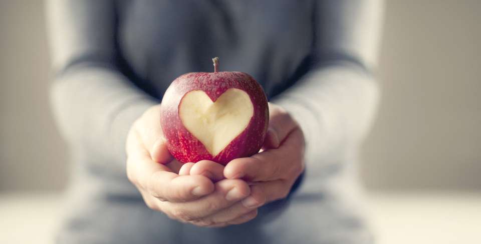 Hands holding an apple with a heart carved into it