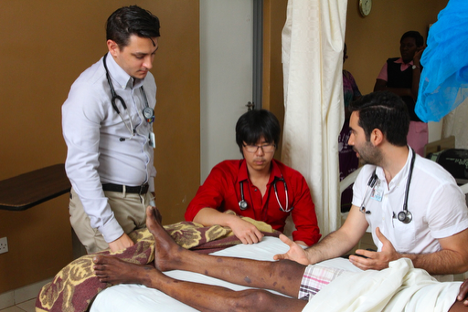 three doctors reviewing a patient's legs in a room