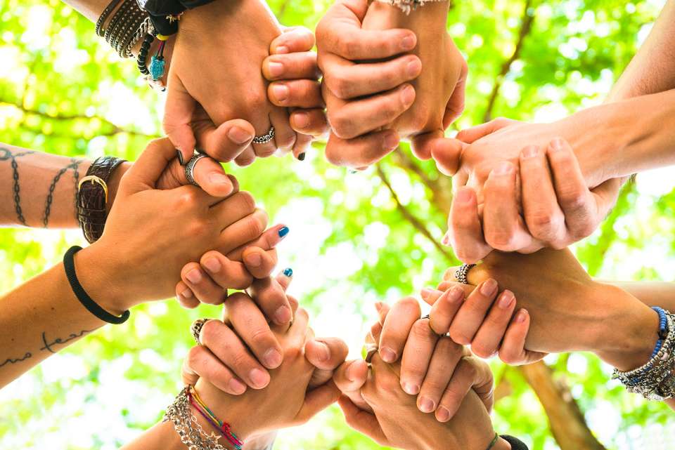 Seven people holding hands in a circle, close-up of just their hands captured from below.