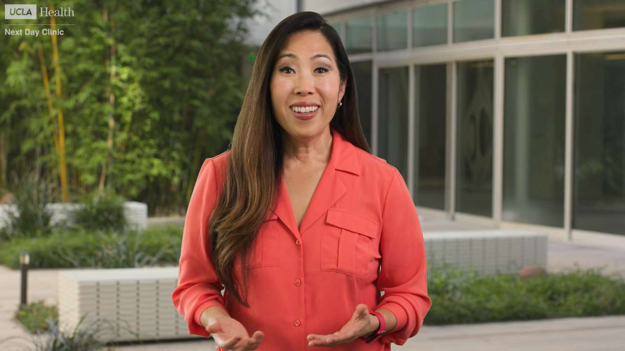 Person in coral blouse gesturing outside a glass office building.