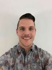 Luke Cunningham wearing a camouflage collared shirt smiling against a white background