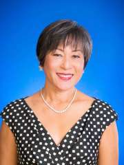 Woman in a polka dot dress with a pearl necklace, against a blue background.