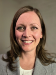 Danielle Spitzmiller with shoulder-length brown hair wearing a light gray blazer and white top, smiling against a plain background.