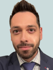 Robert with short dark hair and beard wearing a suit, checkered shirt, and tie, smiling in front of a plain background.