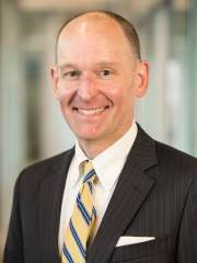 Formal portrait of a man in a suit with a striped tie against a blurred background.