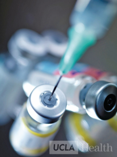 Close-up of a syringe drawing liquid from a vial, with a blurred background and the UCLA Health logo in the corner.