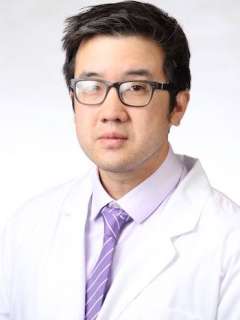 Headshot of Dr. Eric Yang, a man wearing glasses, a white lab coat, and a purple striped tie looking focused.