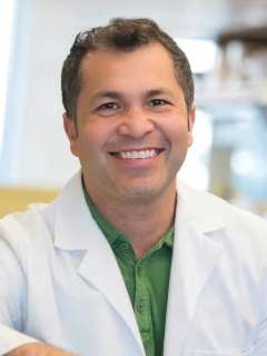 Dr. Hector Aguilar-Carreno sits wearing a lab coat and smiling
