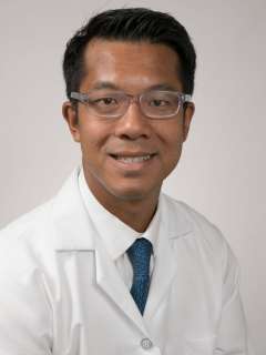  headshot of Dr. Albert Chang, a man with glasses, smiling and wearing a white lab coat and blue tie against a gray background.